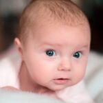 Imagen de un bebé con ojos azules mirando hacia la cámara.