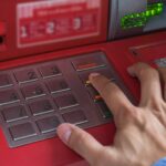 Mano presionando el botón "Cancelar" en un cajero automático rojo, ilustrando su función y precauciones de seguridad.