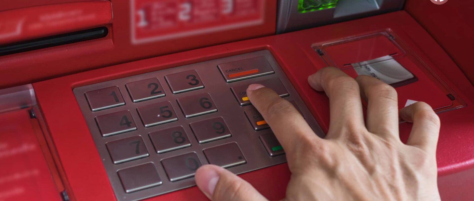 Mano presionando el botón "Cancelar" en un cajero automático rojo, ilustrando su función y precauciones de seguridad.