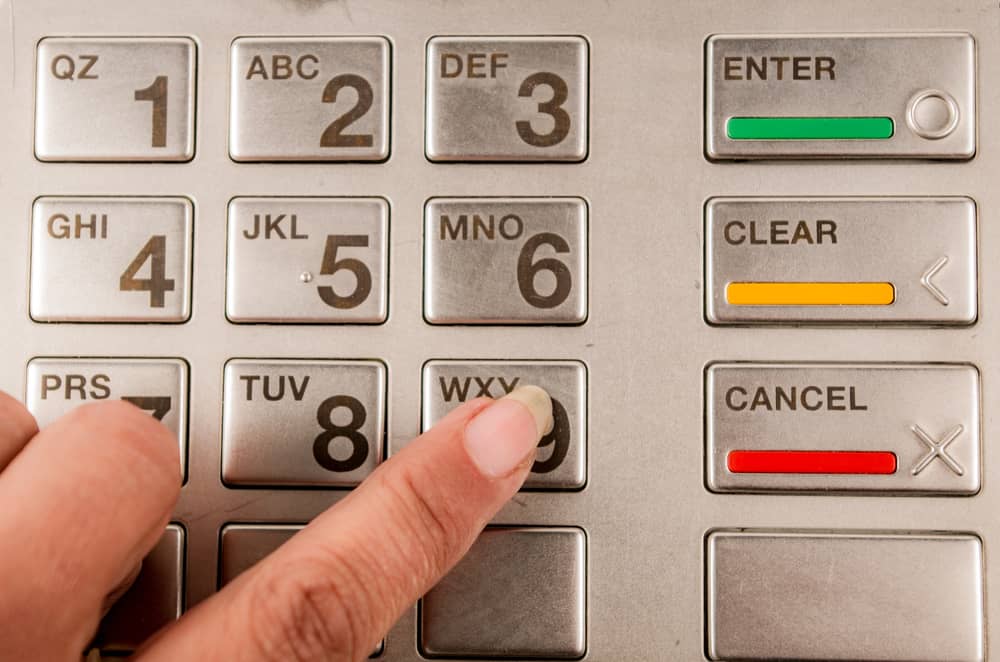 Primer plano del teclado de un cajero automático con un dedo presionando el botón "Cancelar", enfatizando la seguridad en transacciones bancarias.
